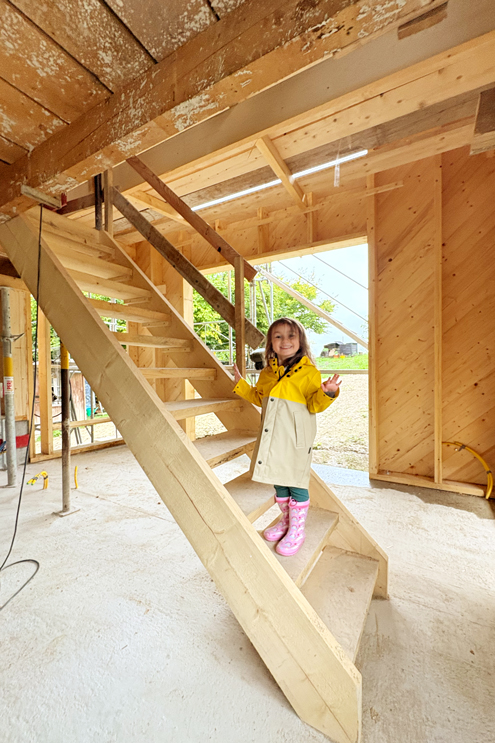 Blick in den neuen Anbau, welcher die Wohnebene erweitern wird. Ausgang in den Garten. Provisorische Treppe Holzbau Roger Gassmann Bülach. Billie mit guter Laune auf der Treppe. Diagonale Holzschalung zur Aussteiffung des Holzbaus. nijo architekten Zürich Nina und Johannes Wick