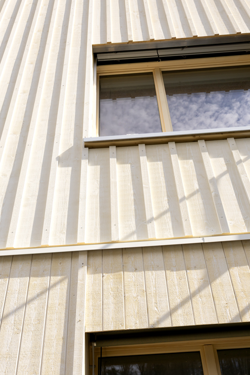 Nahaufnahme Holzfassade Umbau Wohnhaus Affoltern. Das Sockelgeschoss ist glatt geschalt mit sägerauem Täfer, die Obergeschosse haben eine stärker profilierte Fassade mit breiteren Brettern und schattenwerfenden Abdeckleisten. Die gesamte Fassade ist sägerau gehalten und weiss geschlämmt mit Falu Vapen Schwedenfarbe in Stockholmweiss. Holzbau und Holzfassade von Roger Gassmann aus Embrach.  nijo architekten Zürich