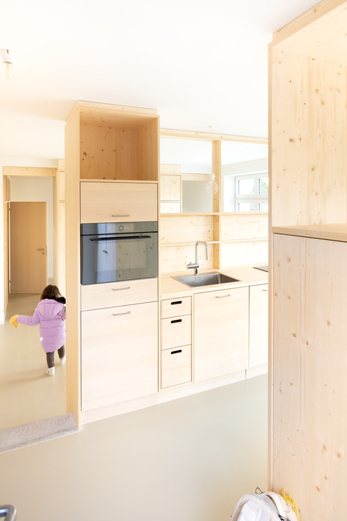Umbau Ausbau Sockel Keller Küsnacht Blick von der Garderobe / Haustüre in den Wohnraum. Der offene Raum erstreckt sich über die ganze Hauslänge und wird durch Holzeinbauten (Küche, Schrank, Regal) in drei Bereiche gegliedert: Küche-Eingang-Essen, Wohnen, Schlafen. Das Bad ist ganz hinten. von hier aus gelangt man auch auf die Verbindungstreppe zum Keller und zum oberen Geschoss. 