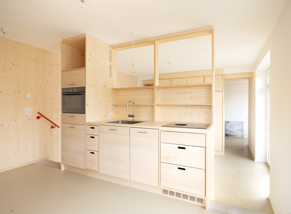Küsnacht Ausbau unbeheizter Keller in Wohnung. Der Eingangsbereich mit Garderobe, Küche und Essecke blieben auf dem Niveau der alten Bodenplatte, damit man von Aussen ebenerdig hinein kommt. Die Küche dient als halboffener Raumteiler zum nachfolgend tiefer gelegten Wohn und Schlafbereich. Hier wurde die Bodenplatte 40cm abgesenkt, die Aussenwände und Fundamente mussten unterfangen / unterbetoniert werden. Der offene Raum soll möglichst fliessend sein, deshalb kann man beidseitig der Küche über zwei Treppenstufen auf die untere Ebene. 